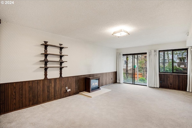 unfurnished living room featuring a textured ceiling, light colored carpet, and wooden walls