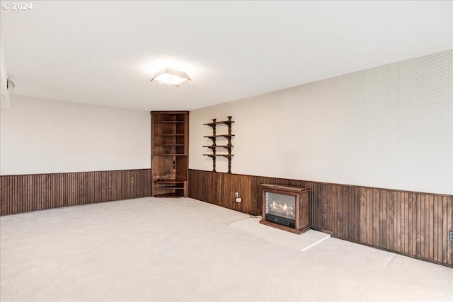 spare room featuring light carpet, a fireplace, and wood walls