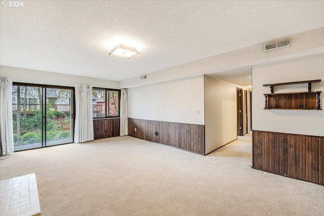 spare room featuring a textured ceiling, light colored carpet, and wooden walls