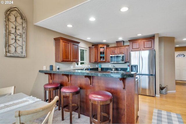 kitchen with light wood-type flooring, stainless steel appliances, a kitchen bar, and kitchen peninsula