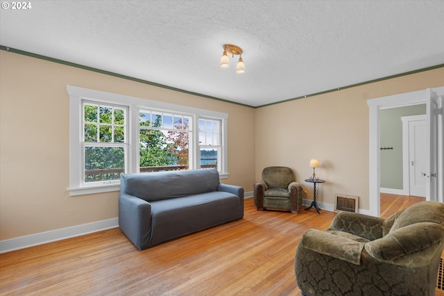 living room featuring light wood-type flooring, ornamental molding, and a textured ceiling