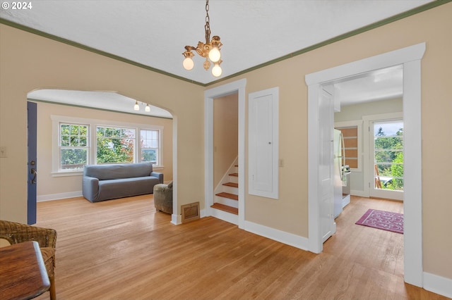 entrance foyer with ornamental molding, light wood-type flooring, and a notable chandelier