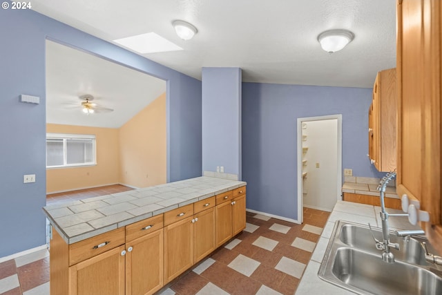 kitchen with kitchen peninsula, vaulted ceiling, ceiling fan, sink, and tile counters