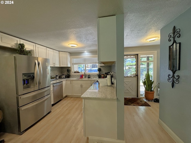 kitchen with light hardwood / wood-style flooring, decorative backsplash, light stone counters, white cabinetry, and stainless steel appliances