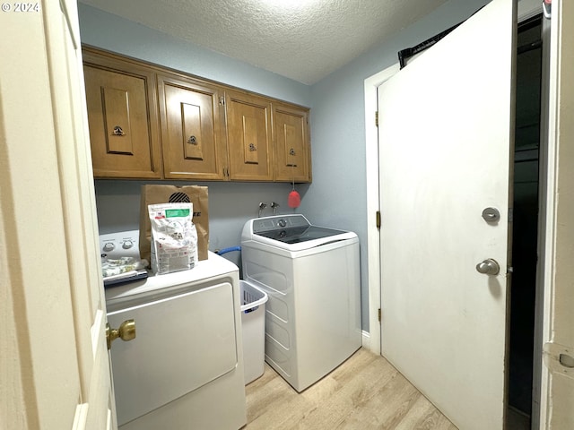 laundry area featuring washing machine and clothes dryer, cabinets, a textured ceiling, and light wood-type flooring