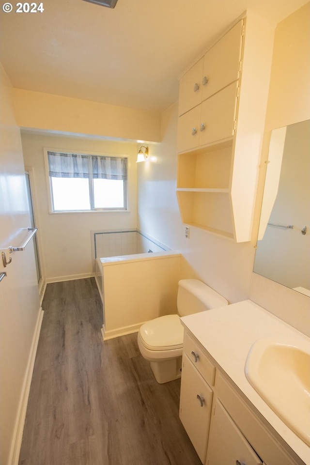 bathroom with baseboards, toilet, wood finished floors, vanity, and a bath