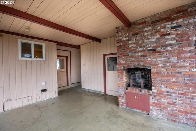 unfurnished living room with a fireplace, beamed ceiling, concrete floors, and wooden walls