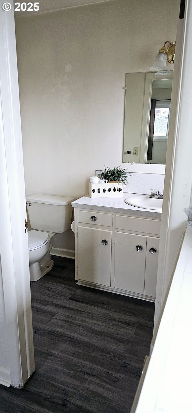 bathroom featuring toilet, baseboards, wood finished floors, and vanity