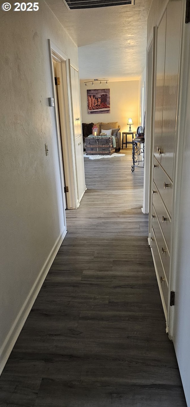 hallway featuring dark wood-type flooring, a textured wall, and baseboards