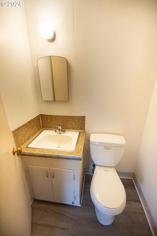 half bath featuring toilet, baseboards, wood finished floors, and vanity