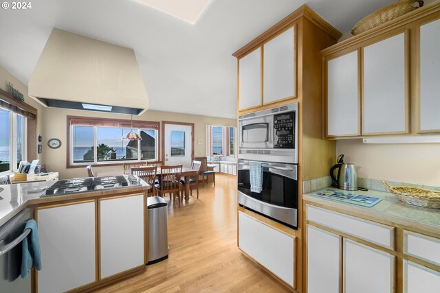 kitchen featuring white cabinets, light hardwood / wood-style flooring, decorative light fixtures, appliances with stainless steel finishes, and range hood