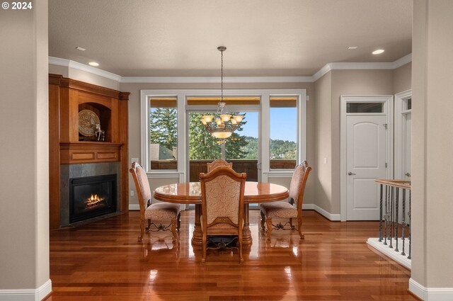 dining area with ornamental molding, a tiled fireplace, a chandelier, and hardwood / wood-style flooring