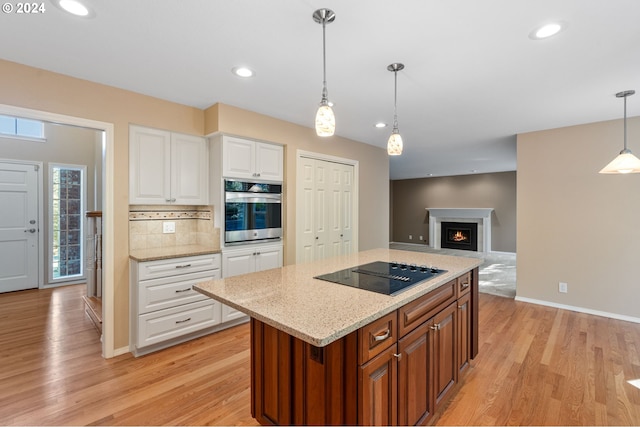 kitchen featuring decorative light fixtures, stainless steel oven, white cabinetry, black electric cooktop, and light wood-type flooring