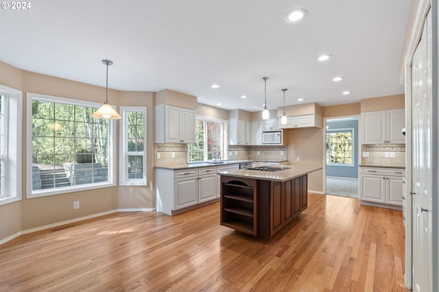 kitchen featuring a wealth of natural light, a center island, white microwave, and white cabinets