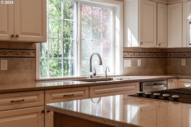 kitchen with plenty of natural light, light stone counters, backsplash, and white cabinets