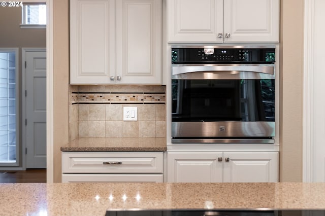 kitchen featuring white cabinets, light stone countertops, oven, and tasteful backsplash