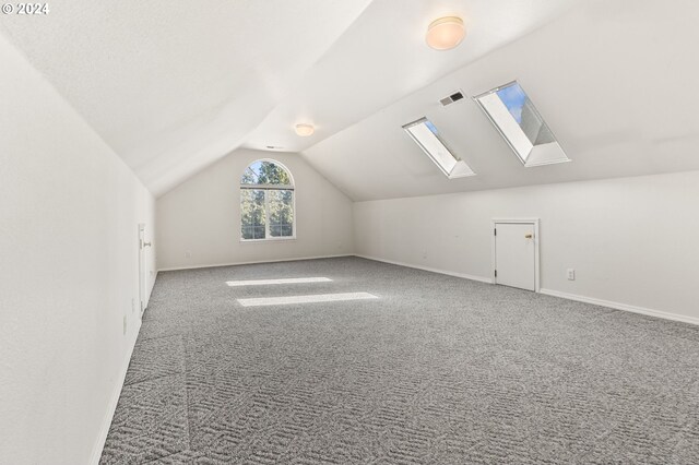 additional living space with vaulted ceiling with skylight and light colored carpet