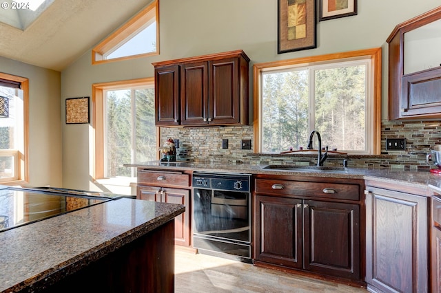 kitchen with backsplash, sink, lofted ceiling with skylight, and black dishwasher