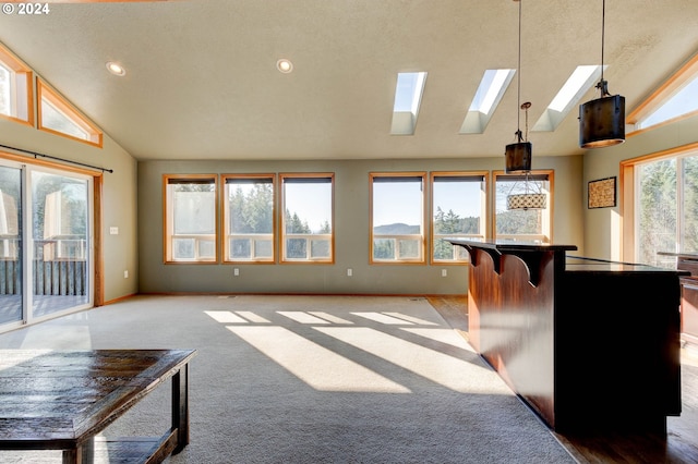 interior space featuring a skylight, high vaulted ceiling, a textured ceiling, decorative light fixtures, and a breakfast bar area