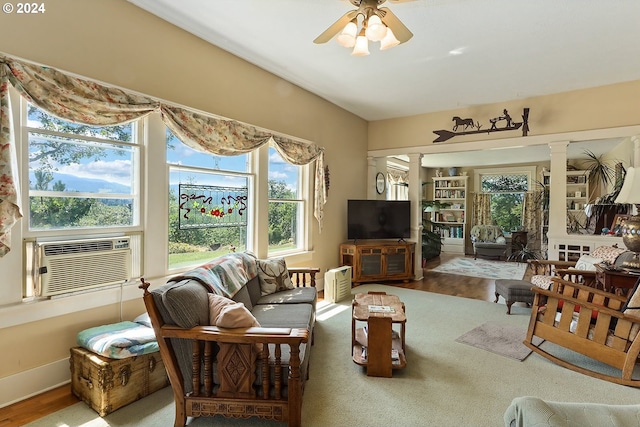 living area featuring a ceiling fan, wood finished floors, cooling unit, baseboards, and ornate columns