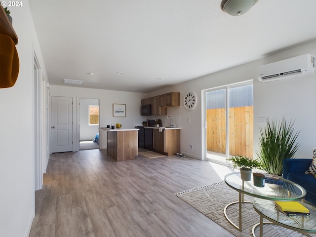 unfurnished living room with sink, a wall mounted air conditioner, light hardwood / wood-style floors, and plenty of natural light