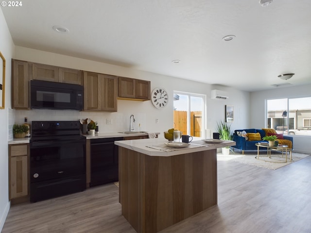 kitchen featuring a wall mounted AC, black appliances, sink, and light wood-type flooring