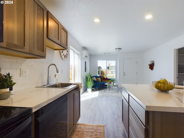 kitchen with a wall unit AC, black dishwasher, sink, light wood-type flooring, and tasteful backsplash