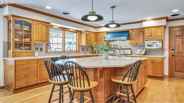 kitchen featuring stainless steel microwave, light hardwood / wood-style floors, a kitchen island, wall chimney exhaust hood, and stove