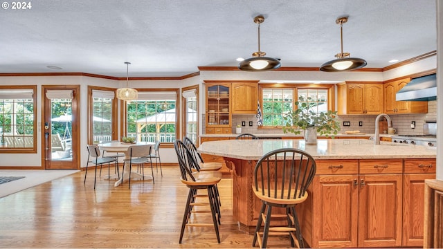 kitchen featuring light stone counters, pendant lighting, wall chimney range hood, light hardwood / wood-style floors, and tasteful backsplash