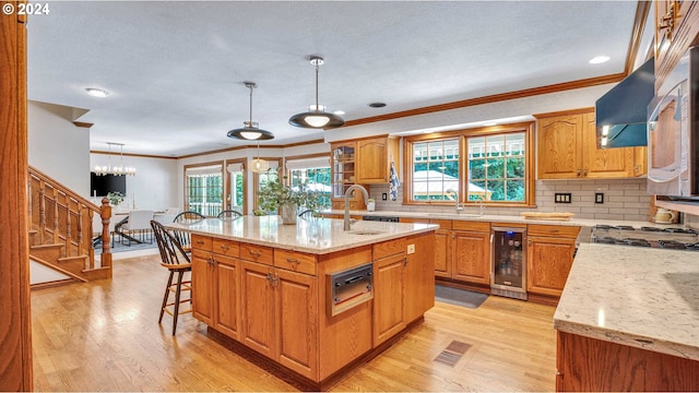 kitchen with light hardwood / wood-style flooring, pendant lighting, a center island with sink, wine cooler, and backsplash