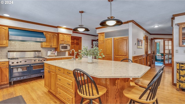 kitchen featuring wall chimney exhaust hood, an island with sink, decorative backsplash, hanging light fixtures, and appliances with stainless steel finishes