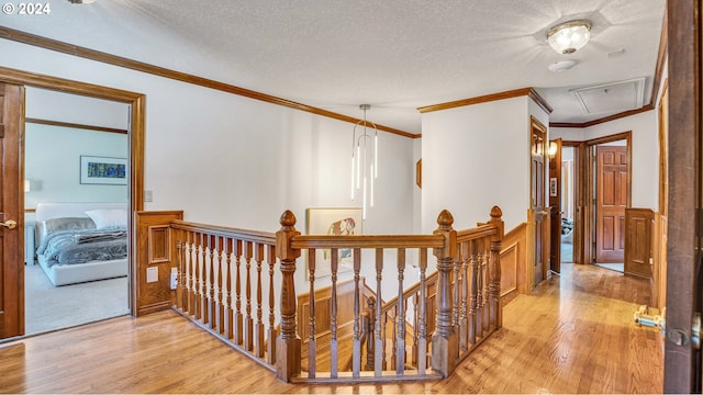 corridor with a textured ceiling, crown molding, and light hardwood / wood-style flooring