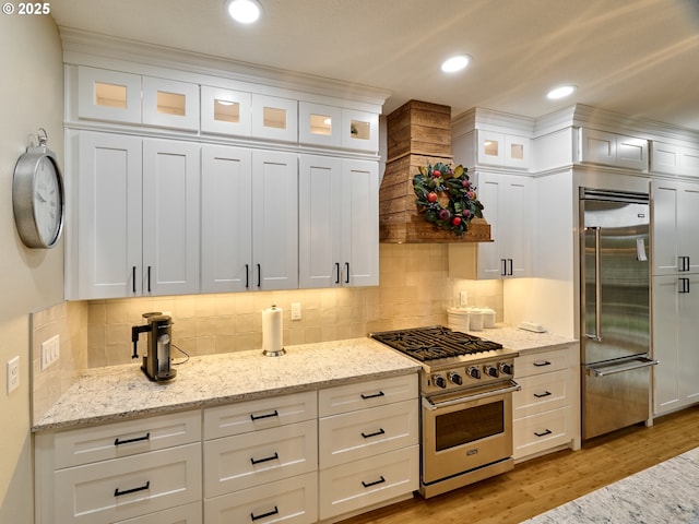 kitchen with high end appliances, white cabinetry, light wood-type flooring, and light stone counters