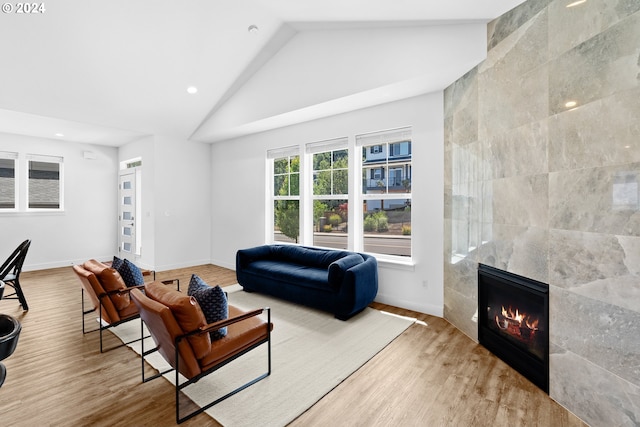 living room featuring tile walls, high vaulted ceiling, a fireplace, and light hardwood / wood-style floors