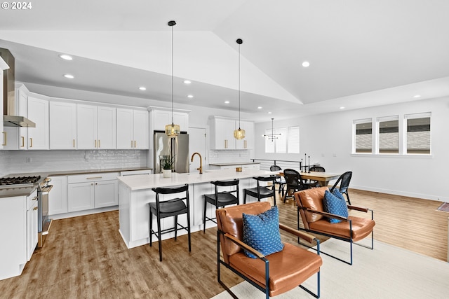 kitchen featuring appliances with stainless steel finishes, decorative light fixtures, white cabinets, light hardwood / wood-style flooring, and a kitchen island with sink