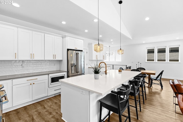 kitchen featuring white cabinets, a center island with sink, a breakfast bar area, stainless steel appliances, and decorative light fixtures