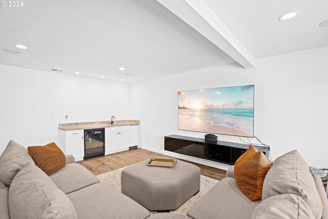 living room featuring indoor wet bar, light hardwood / wood-style flooring, wine cooler, and beamed ceiling