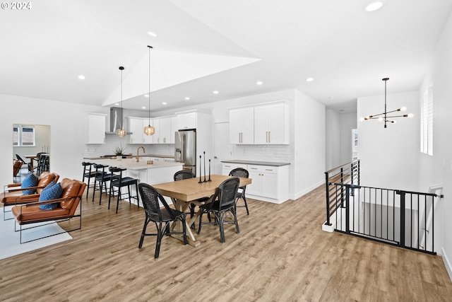 dining area featuring sink, vaulted ceiling, light hardwood / wood-style flooring, and an inviting chandelier