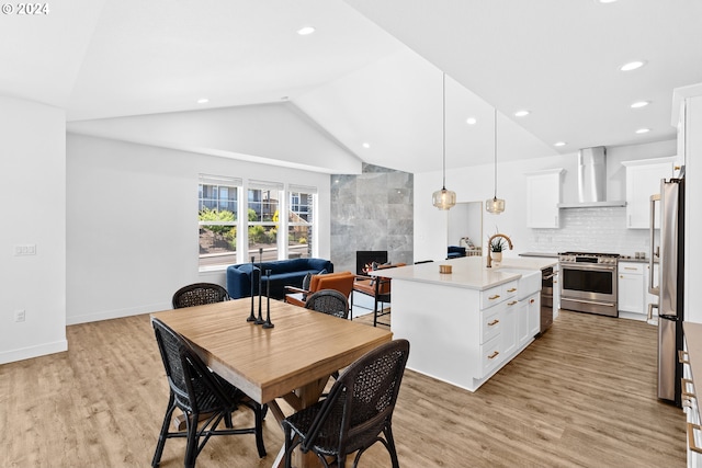 dining area with light hardwood / wood-style floors, a high end fireplace, sink, and vaulted ceiling