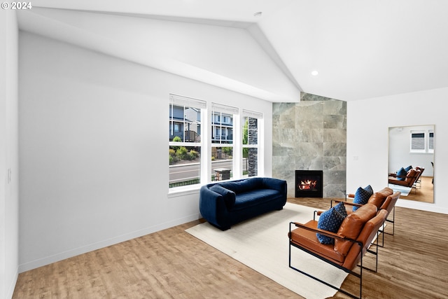 living room featuring tile walls, a tile fireplace, vaulted ceiling, and light hardwood / wood-style floors