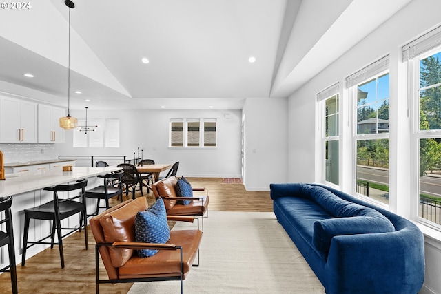 living room featuring light hardwood / wood-style floors, a notable chandelier, and vaulted ceiling