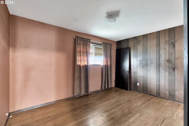 empty room featuring a textured ceiling, wooden walls, and light hardwood / wood-style flooring