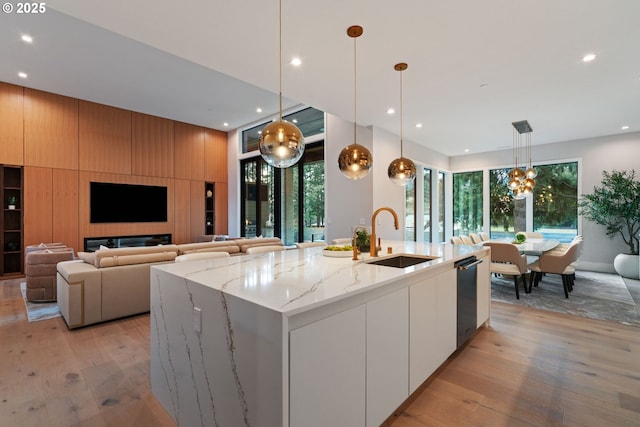 kitchen with a spacious island, sink, decorative light fixtures, light stone countertops, and white cabinets