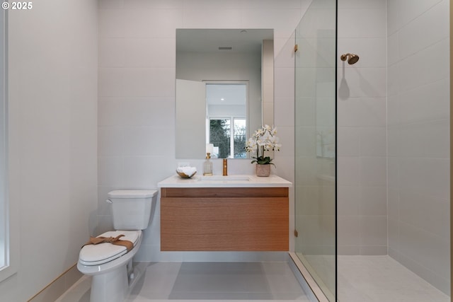 bathroom with vanity, tile walls, toilet, and tiled shower