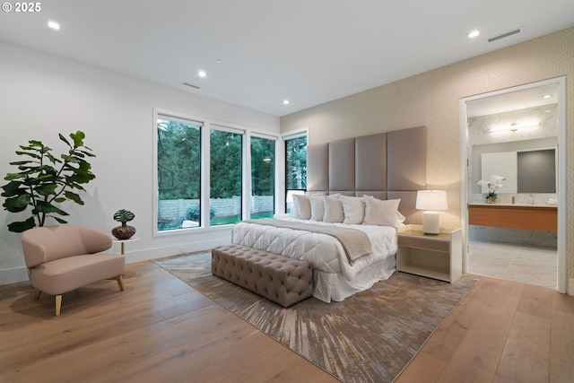 bedroom with connected bathroom and light hardwood / wood-style floors