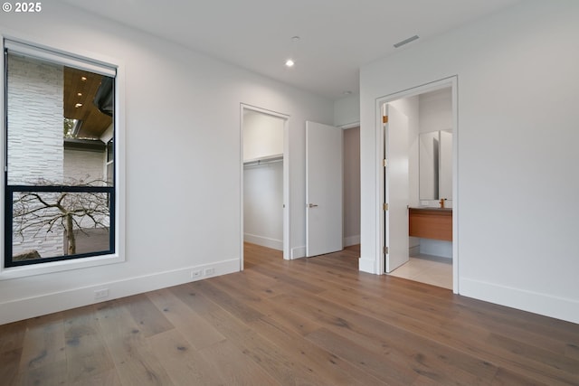 unfurnished bedroom featuring hardwood / wood-style floors, a spacious closet, a closet, and ensuite bathroom