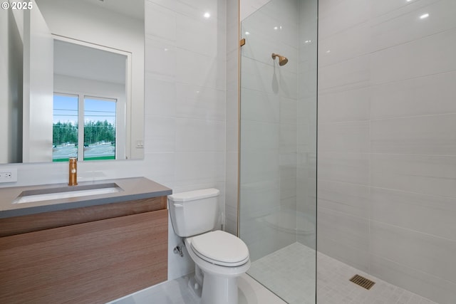 bathroom with tiled shower, vanity, toilet, and tile walls