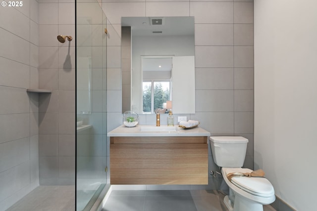 bathroom featuring tiled shower, vanity, toilet, and tile walls