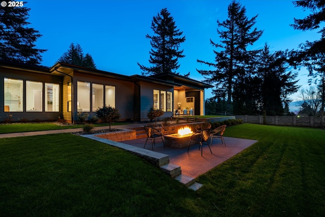 back house at dusk featuring an outdoor fire pit, a patio area, and a lawn