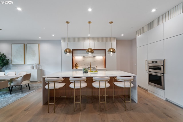 kitchen with decorative light fixtures, a breakfast bar, double oven, and light wood-type flooring